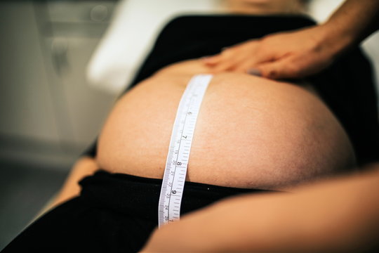 pregnant woman with midwife. Beautiful body of pregnant woman using measuring tape to check baby development, healthcare and wellness. Health well being pregnancy lifestyle.