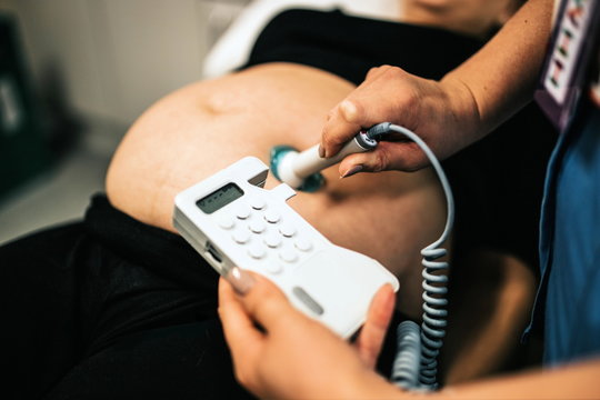 Close up of ultrasound examination of the fetus. Pregnant woman in gynecological clinic. Prenatal testing of young blond woman with hands of doctor. ultrasound scanner in hands of doctor examining her