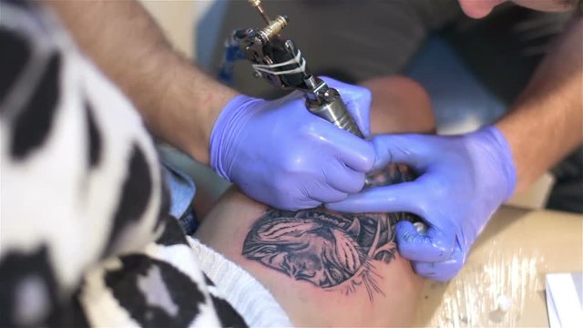 Professional tattoo artist makes tattoo on woman's leg. Tattoo parlor. Patterning on skin. Body art