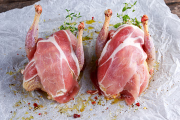 Ready to cook raw seasoned partridges with bacon on crumpled paper.