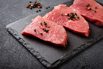  Raw  beef steak on a dark  board. Fresh raw meat with spices.