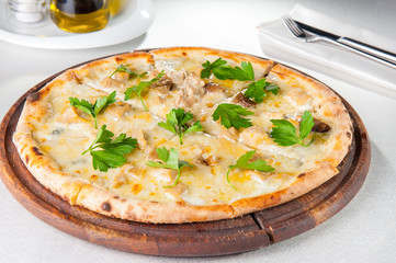 Close up gourmet pizza with gorgonzola and porcini white mushrooms decorated with parsley leaves on the wooden board on the served restaurant table