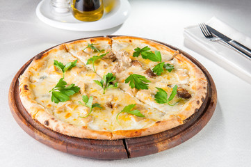 Close up gourmet pizza with gorgonzola and porcini white mushrooms decorated with parsley leaves on the wooden board on the served restaurant table