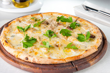 Close up gourmet pizza with gorgonzola and porcini white mushrooms decorated with parsley leaves on the wooden board on the served restaurant table