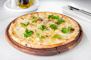 Close up gourmet pizza with gorgonzola and porcini white mushrooms decorated with parsley leaves on the wooden board on the served restaurant table