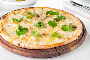 Close up gourmet pizza with gorgonzola and porcini white mushrooms decorated with parsley leaves on the wooden board on the served restaurant table