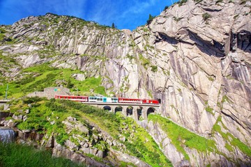 Train on the railway bridge Teufelsbrucke over Reuss river in St. Gotthard mountain range of Swiss...