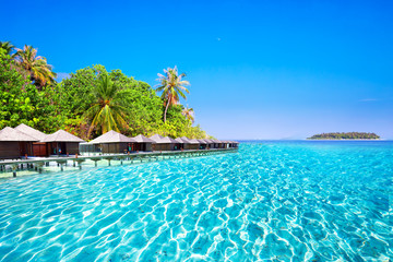 Overwater bungalows on tropical island with sandy beach, palm trees and beautiful lagoon