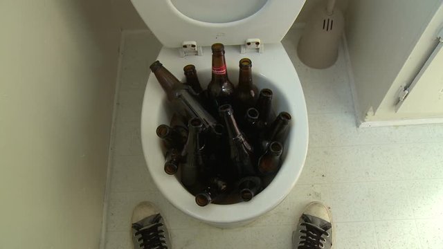 Beer Bottle Toilet Flush. Funny static point of view (POV) shot of a man standing above a toilet filled with a bunch of beer bottles, then flushes.