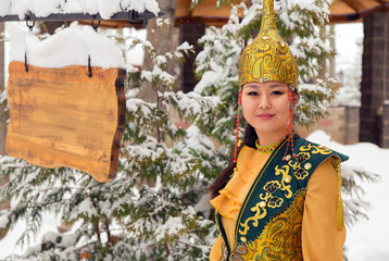 Woman in Kazakh costume.
Smiling young Asian woman in Kazakh national costume outdoors. Conifers covered with snow in the background.