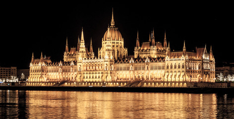 Fototapeta na wymiar Night view of illuminated historical building of Hungarian Parliament, aka Orszaghaz, with typical symmetrical architecture and central dome on Danube River embankment in Budapest, Hungary, Europe. It
