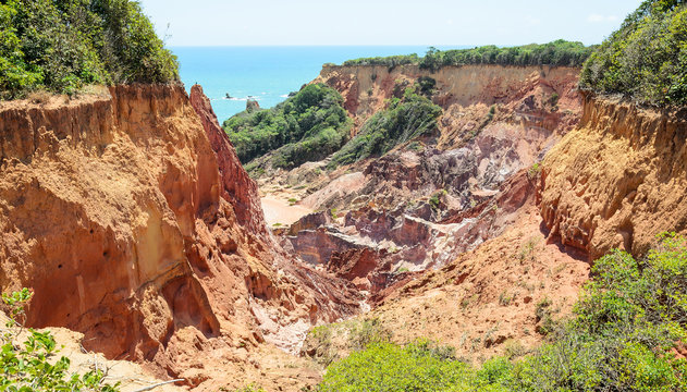 Canyon of cliffs with many stones sedimented by time, rocks with red and yellow colors and the sea in the background. Cliffs of Coqueirinho beach, PB - Brazil.