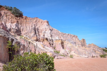 Fototapeta premium Canyon cliffs with many rocks sedimented by time, rocks with red and yellow colors. Cliffs of Coqueirinho beach, PB - Brazil.