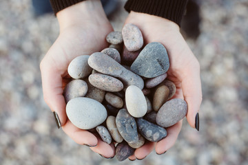 Woman holding smooth pebbles on rocky beach