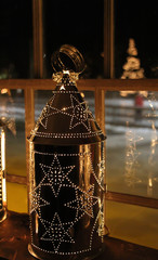 shiny tin lantern shining in a window with the reflection of a holiday tree in the background