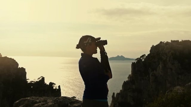 Female hiker looking in binoculars enjoying spectacular view by the sea, Calanques, France