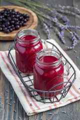 Black currant, greek yogurt, honey and lavender smoothie in glass jar with berries and flowers on background, vertical