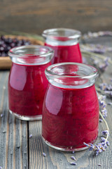 Black currant, greek yogurt, honey and lavender smoothie in glass jar with berries and flowers on background, vertical