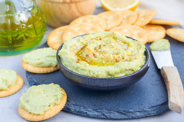 Healthy avocado hummus sprinkled with olive oil, paprika and sesame, served with crackers, horizontal