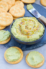 Healthy avocado hummus sprinkled with olive oil, paprika and sesame, served with crackers, vertical