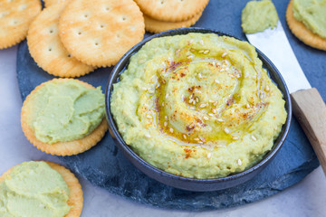 Healthy avocado hummus sprinkled with olive oil, paprika and sesame, served with crackers, horizontal