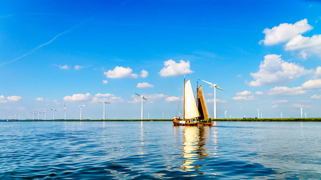 Two Historic Wooden Botter Boats in Full Sail near a Wind Farm along the Shore of Veluwemeer in the Netherlands