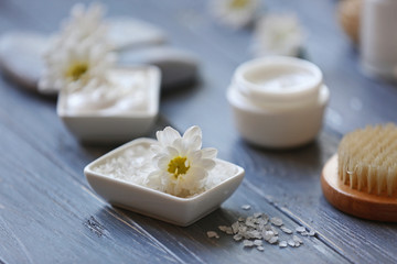 Fototapeta na wymiar Spa concept. Nourishing cream and daisy flowers on grey wooden table
