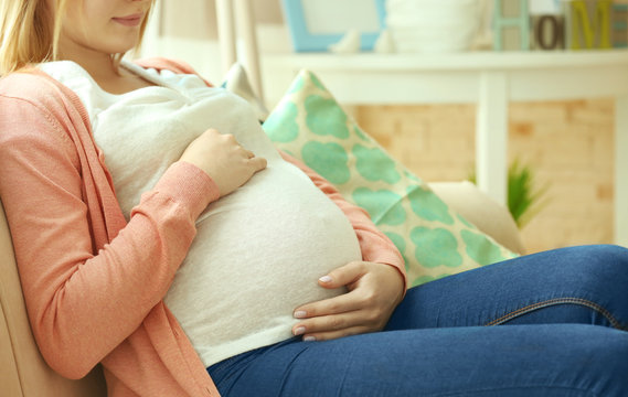 Pregnant woman sitting on couch at home, closeup