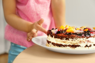 Little girl tasting sweet cake left on kitchen table, close up view