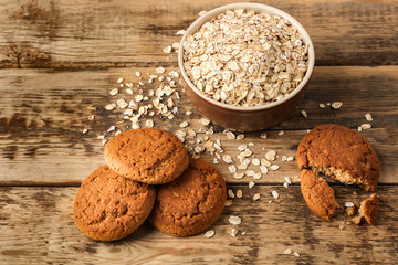 Oatmeal cookies and bowl with groats on wooden background