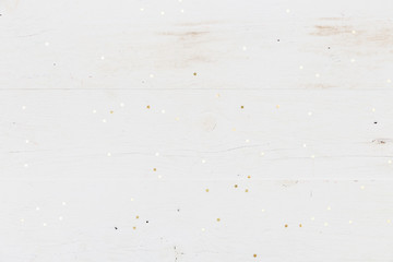 Small golden stars confetti on white wooden background.