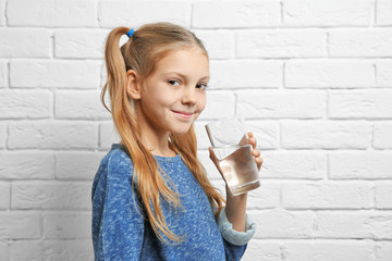 Cute pretty girl with glass of water near brick wall