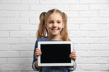 Cute girl with tablet computer near brick wall