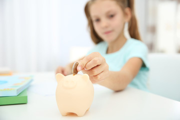 Obraz na płótnie Canvas Cute girl putting coins into piggy bank at home, closeup