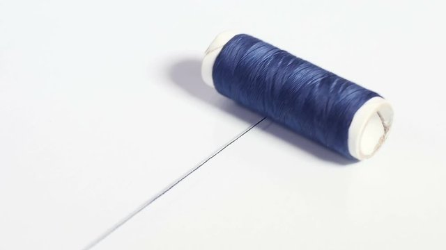 Isolated spool of dark blue thread rolling on white surface, white paper bobbin, sewing accessories, tools for tailoring, haberdashery. Close up, shallow DOF, 4K Ultra HD.