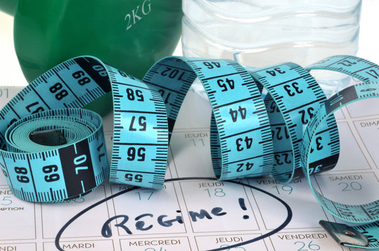 Le mot régime écrit sur un calendrier avec un centimètre souple, une haltère et une bouteille d'eau