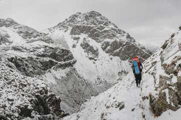 Fototapeta premium Climber walking on a steep snow-covered slope in the mountains on the background of a cliff and the abyss. The concept of risk and adventure outdoor