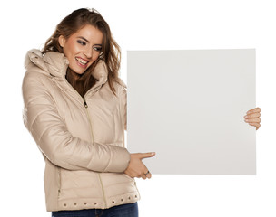 young woman in winter jacket holding a blank board for advertisement