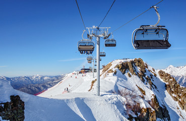 Chair ski lifts and ski tracks in Sochi winter mountain ski resort on the blue sky and snowy peaks...