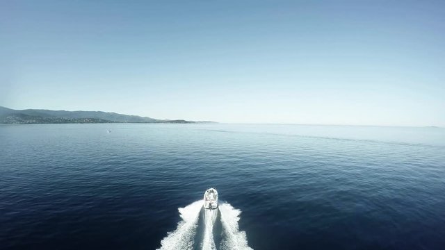 Aerial flight bird view following fancy speedboat moving fast over quiet flat sea very beautiful day white fast ship moving straight over blue water in background showing shore island and blue sky 4k
