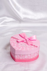 Pink heart shaped gift box with bow over white satin