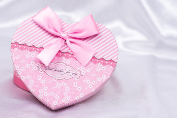 Heart shaped gift box with bow over white satin