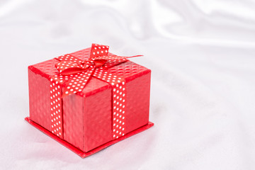 Red gift box with bow on the white satin background
