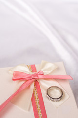 White gift box with red bow and golden wedding ring