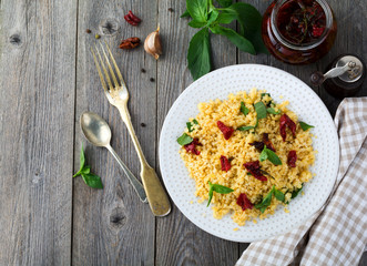 Bulgur with dried tomatoes and basil on an old wooden background. Vegetarian dish.Rustic style. Selective focus.Top view.