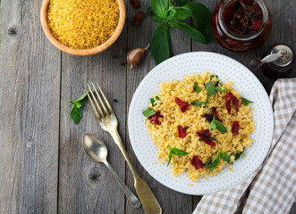Bulgur with dried tomatoes and basil on an old wooden background. Vegetarian dish.Rustic style. Selective focus.Top view.