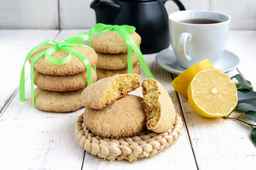 Shortbread lemon flavored cookies: a broken and connected green ribbon for a gift. Teapot and fresh lemon on a white wooden background. 