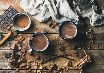 Hot chocolate with cinnamon sticks, anise, nuts and cocoa powder on rustic wooden background, top view, horizontal composition