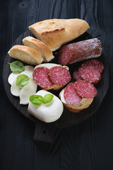 Black wooden serving board with salami and cheese bruschetta