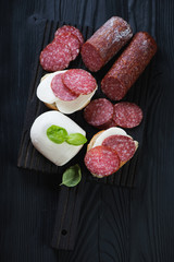 Sliced salami with mozzarella over black wooden background